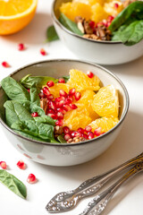Bright fruit salad close-up. Salad of oranges, pomegranate, spinach and nuts in a bowl on a white plate. Healthy diet food, vegetarian food.