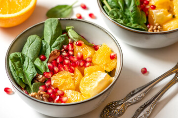 Bright fruit salad close-up. Salad of oranges, pomegranate, spinach and nuts in a bowl on a white plate. Healthy diet food, vegetarian food.