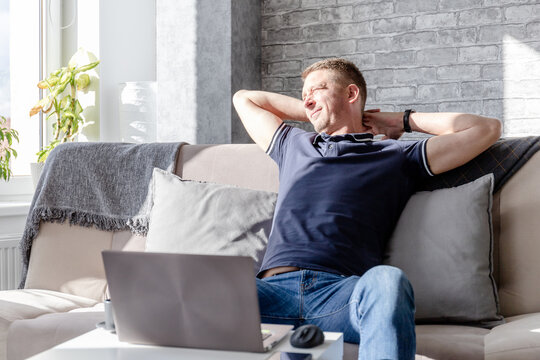 middle-aged man stretches while sitting on the couch after work at the laptop