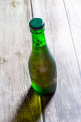 Blond beer on a green bottle closed on a wooden background