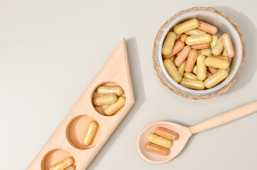 Herb in capsules in wooden bowl on pastel beige background. Beauty products for face and body skin care