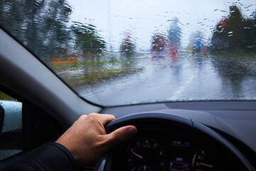 A man drives a car under a heavy drizzle, autumn weather