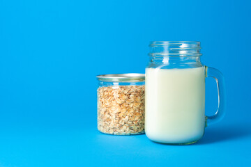 Glass cup of milk and glass box of oat flakes on blue background