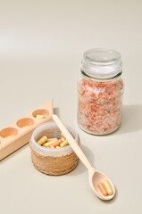 Herb in capsules in wooden bowl on pastel beige background. Beauty products for face and body skin care