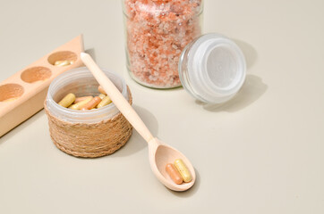 Herb in capsules in wooden bowl on pastel beige background. Beauty products for face and body skin care