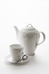 Close up view of tea kettle and tea cup with spoon on white back