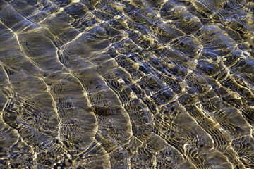 Light ripples on the surface of the water and the reflection of the sandy bottom, illuminated by the sun. Natural background for graphic designs.