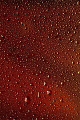 Close up view of cold drops on the glass of beer background. Texture of cooling alcohol drink with macro bubbles on the glass wall. Fizzing or floating up to top of surface. Dark brown colored.