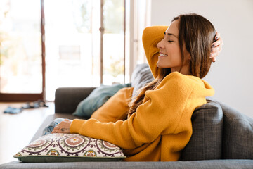 Beautiful caucasian woman smiling while sitting on sofa in apartment