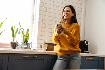 Beautiful caucasian woman smiling and using cellphone in apartment