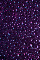 Close up view of cold drops on the glass of beer background. Texture of cooling alcohol drink with macro bubbles on the glass wall. Fizzing or floating up to top of surface. Dark purple colored.