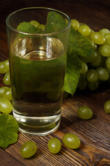 Glass of grape juice and bunch of sweet green grape on dark wooden table.
