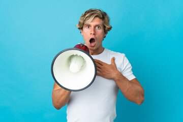 English man over isolated blue background shouting through a megaphone with surprised expression