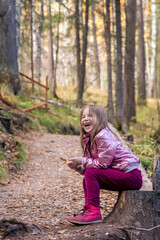 Cute girl in the autumn forest sits on the stump
