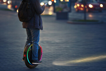 Man riding fast on electric unicycle on city street at night with diode headlights. Mobile portable...
