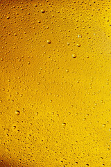 Close up view of cold drops on the glass of beer background. Texture of cooling alcohol drink with macro bubbles on the glass wall. Fizzing or floating up to top of surface. Golden colored.