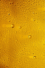 Close up view of cold drops on the glass of beer background. Texture of cooling alcohol drink with macro bubbles on the glass wall. Fizzing or floating up to top of surface. Golden colored.