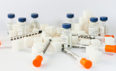 Sugar addiction, insulin resistance, unhealthy diet, sugar cubes pyramid, bottles of insulin and syringe for vaccinationon white background, diabetes protection medical concept, top view.