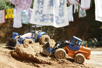 Children's plastic toy trucks on the sand with clothes hanging on the background