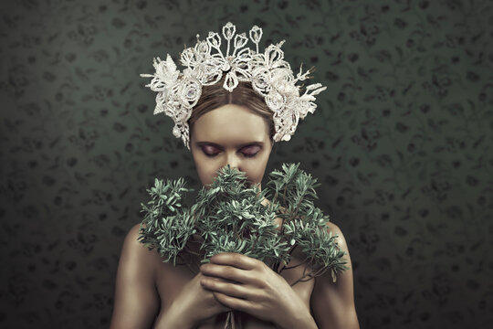 Beautiful young blonde woman with a traditional tembleque headdress, holding flowers towards her face, in front of a grey flower pattern wallpaper
