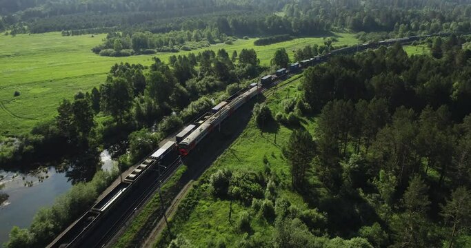 Freight long train carries with cargo carriages in wild mountains landscape through a difficult part of Trans Siberian railways. Aerial drone wide view at summer day.