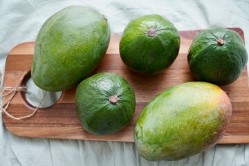 Green three avocado and mango on a wooden chopping board against a green background. Healthy food. Style of life. Meals for vegans. Vegetable table