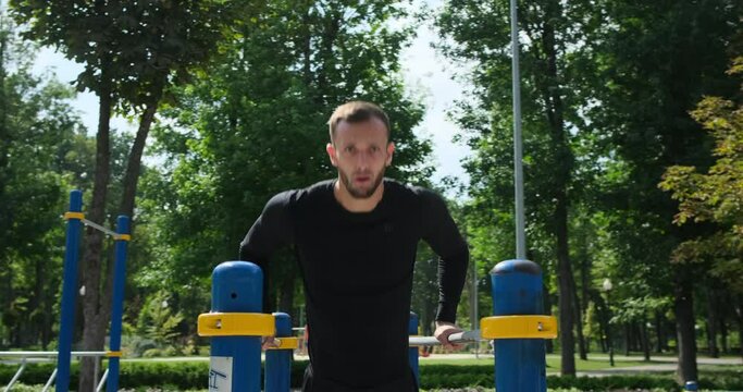 Man in sportswear doing triceps dip exercise on parallel bars at park