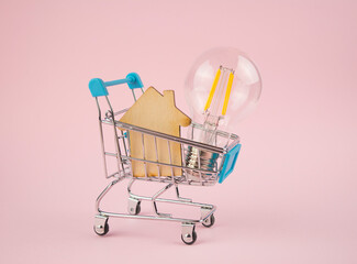 Business concept. Lamp with a wooden house in a shopping cart on a pink background. Buying a home....