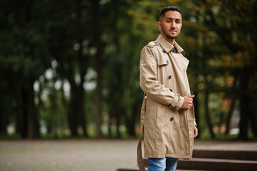 Stylish kuwaiti man at trench coat walking at park.