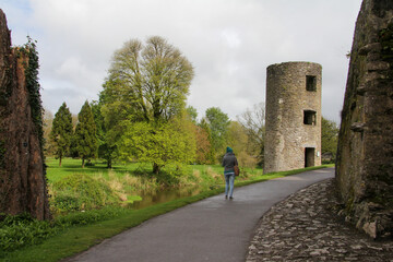 Fototapeta na wymiar Stone tower in a park with vegetation and girl walking on an asphalt road