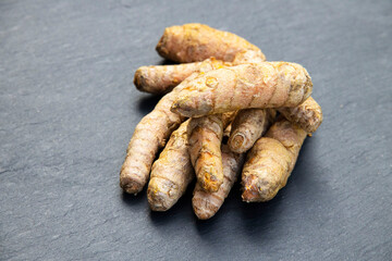 Turmeric powder in a wooden spoon and roots on a dark table (curcuma longa), Kurkuma