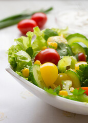 Green salad with red and yellow tomatoes and fresh vegetables in a white bowl