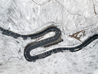 Obraz premium Winding road through the forest, from high mountain pass, in winter time. Aerial view by drone. Romania