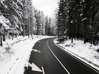 Fototapeta premium Winding road through the forest, from high mountain pass, in winter time. Aerial view by drone. Romania
