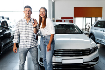 Young happy couple just bought a new car in a dealership