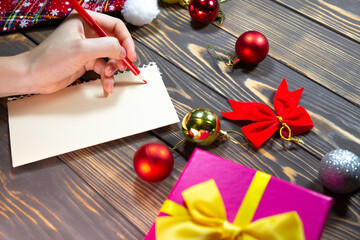 Woman is writing Christmas postcards. Greetings with holidays. Happy new year time. Congratulations to friends and family. Decorations on wooden table. Cozy mood. Copy space place.