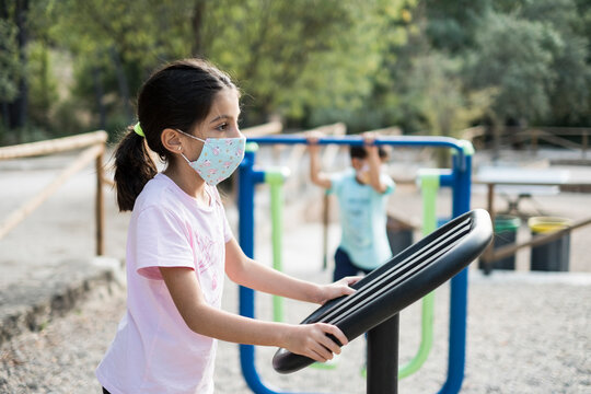 Girl with surgical mask plays in the park with her brother in the background