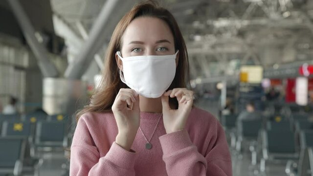 Portrait Of A Woman Put On Medical Mask Looking Straight At Camera In Airport Terminal Preventing Herself From Coronavirus. People Staying In A Queue For Boarding On Plane. Pandemic Covid Concept.