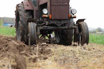 Fototapeta na wymiar Old Soviet 4x4 wheeled brown tractor on the field front view close up, soil cultivation on an autumn day on grass background, countryside agriculture farming mechanization