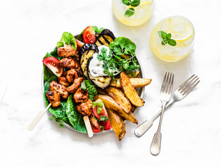 Teriyaki chicken skewers, roasted potatoes, vegetables, grilled eggplant and lemon mint cocktail - delicious appetizer plate, tapas on a light background, top view