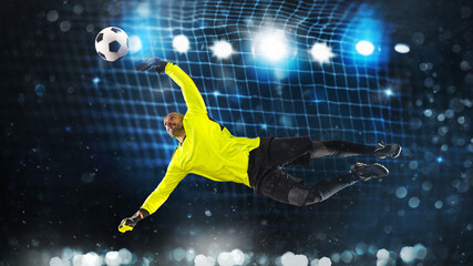 Soccer goalkeeper, in fluorescent uniform, that makes a great save and avoids a goal on a dark blue...