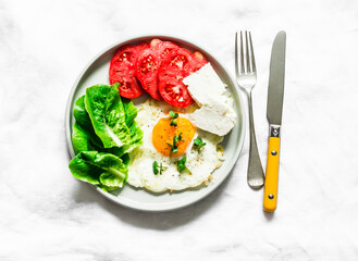 Breakfast, snack, tapas - fried egg, ripe red tomatoes, greek sheep cheese, green salad on a light background, top view