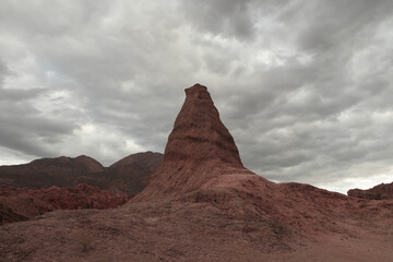 Fototapeta na wymiar Geology. View of the sandstone and red rocky formation and mountains in the arid desert under a cloudy sky.