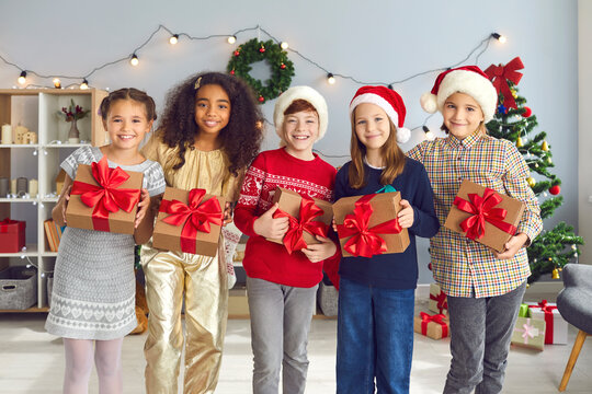 Happy Diverse Kids Holding Christmas Presents Standing In Cozy Living-room During Party At Home