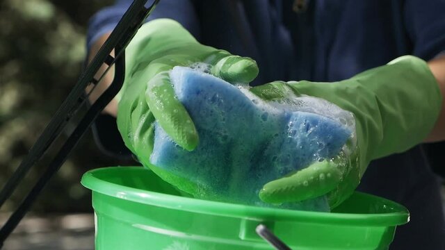 Hand squeezes a blue sponge in a green Bucket of water for a car wash, Image with car care content on a summer sunny day