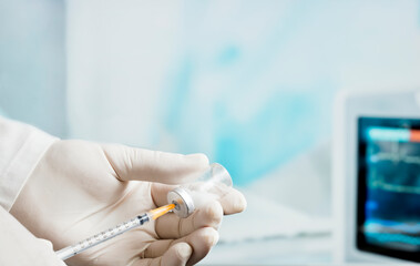 Syringe in the doctor's hand, (focus on orange needle cannula) hospital operating room background.
