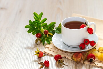 A Cup of tea on a napkin with fresh rosehip berries on a wooden surface 