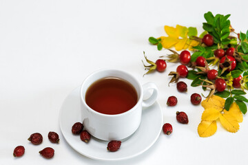 a white Cup of rosehip tea on a white surface, next to it are dried and fresh rosehip berries, a place for text