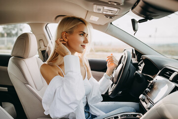 Young blonde woman driver, sitting in a car, looking to rear view window.