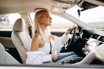 Young blonde woman driver, sitting in a car, looking to rear view window.